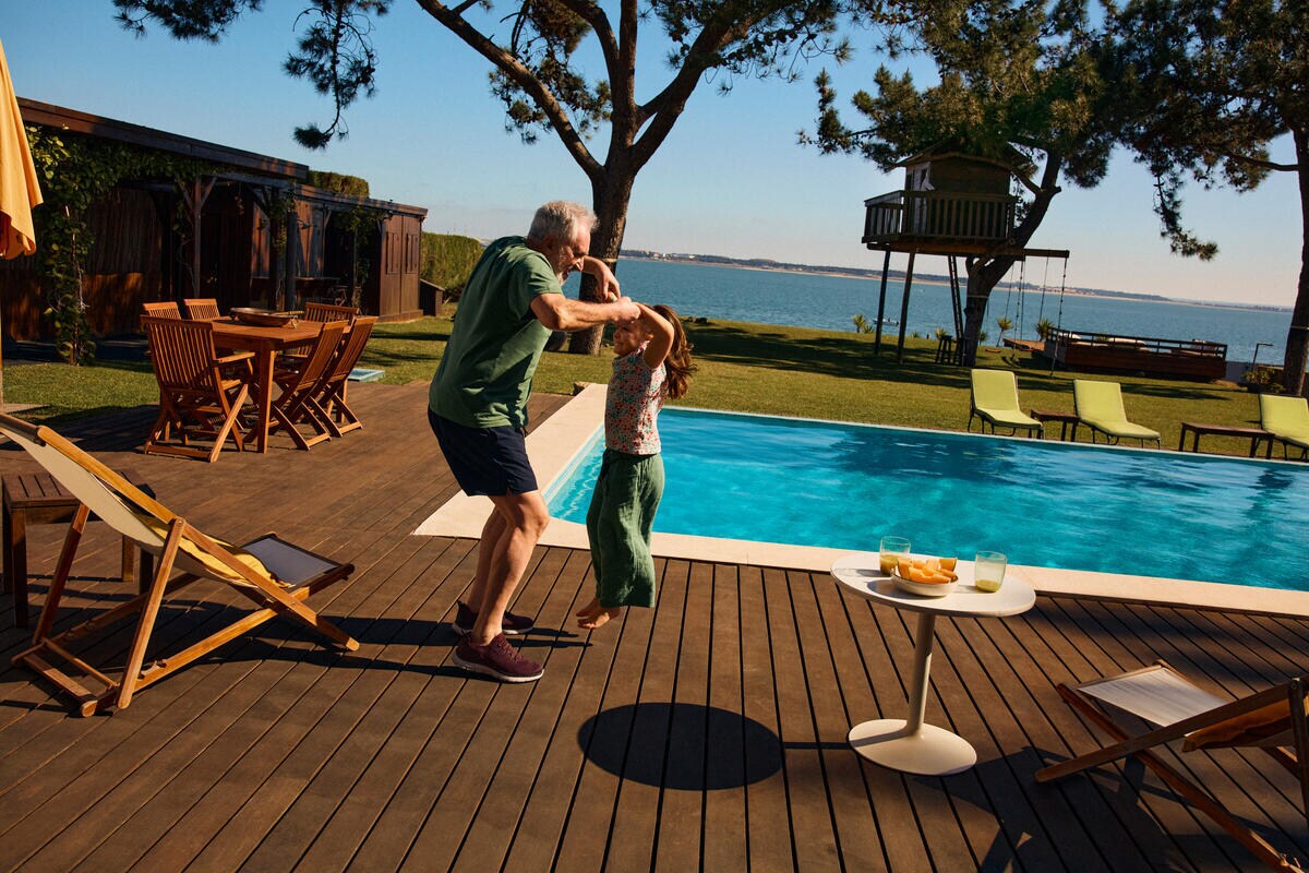 An older man is playing with a joyful girl. He's holding her hands as she jumps.